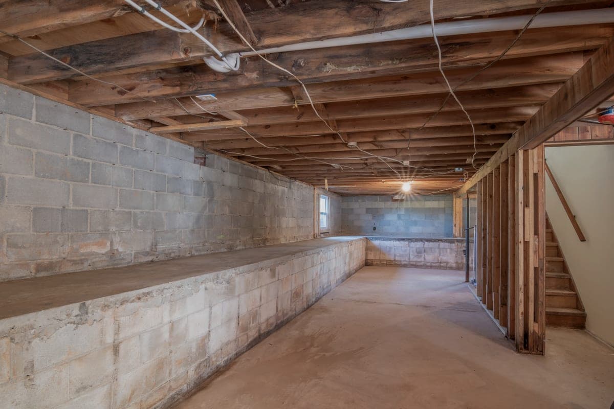 An empty basement with concrete walls, exposed wooden beams and stairs