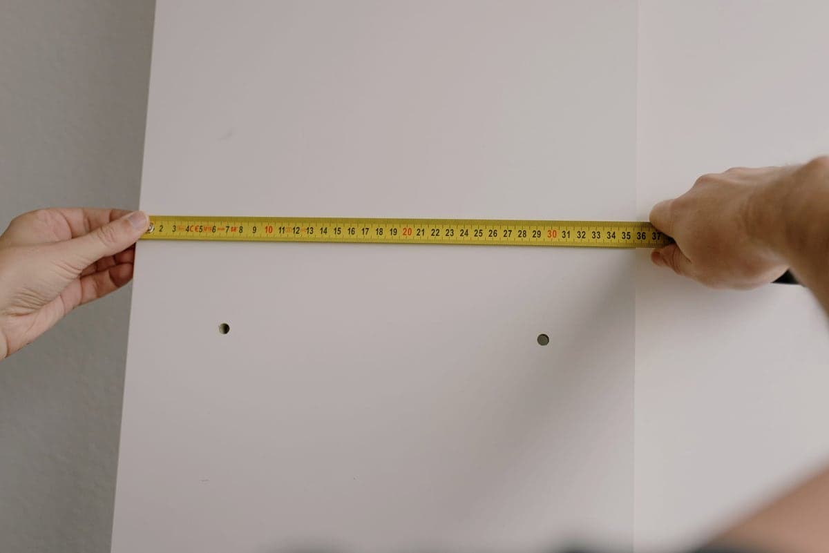 A tape measure and pencil against a wall being marked out for shelving