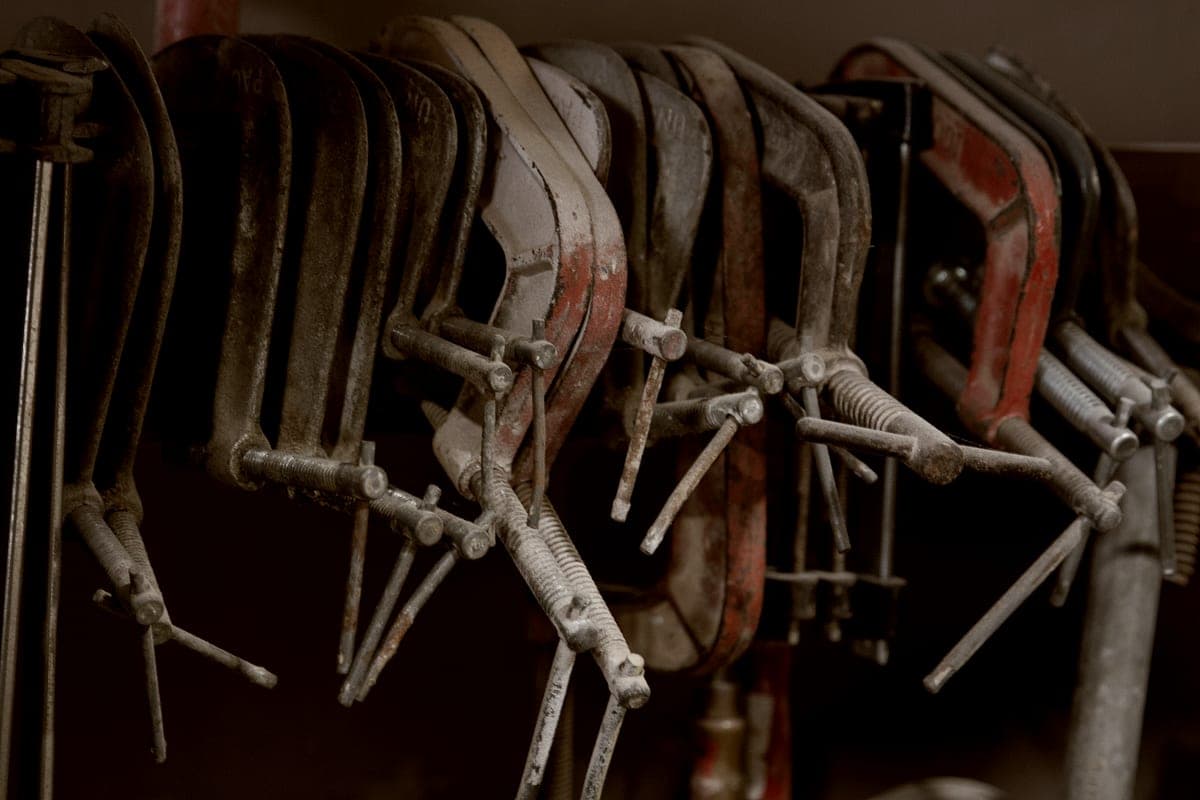 A row of steel clamps hanging along a horizontal workshop rail