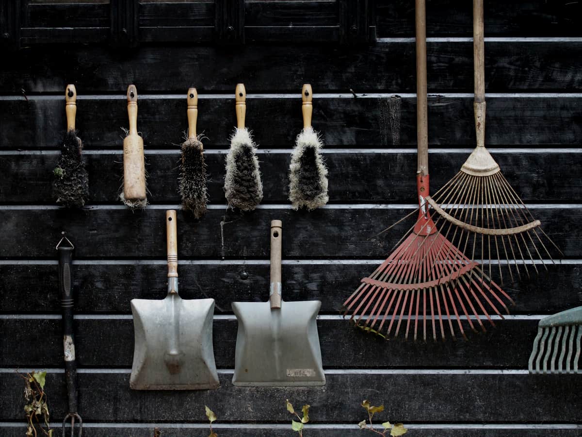 Garden tools hanging in a row on a dark horizontal slatted wooden wall